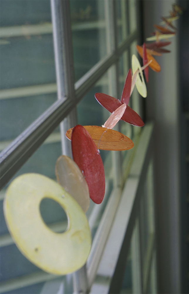 Capiz Shell Strands 72 Inch Long Flame, showcasing vibrant shades of spice, brown, orange, and yellow in a decorative display hanging by a window.