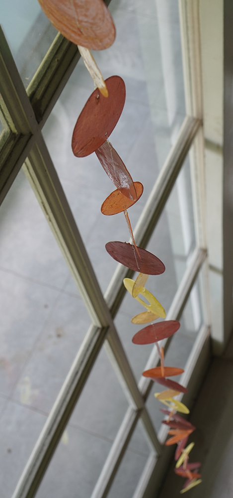 Capiz Shell Strands 72 Inch Long Flame, featuring a beautiful arrangement of colored shell discs in spice, orange, and yellow, elegantly draped by a window.