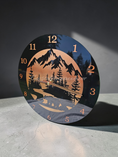 Load image into Gallery viewer, 11.5 inch round black acrylic wall clock with a hand-painted metallic bronze-to-copper gradient. The design features a black silhouette of a black bear, fir trees, and a mountain range with copper numerals and hands.