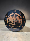 Load image into Gallery viewer, 11.5 inch round black acrylic wall clock with a hand-painted metallic bronze-to-copper gradient. The design features a black silhouette of a black bear, fir trees, and a mountain range with copper numerals and hands.