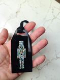 Load image into Gallery viewer, A black gift tag with a black strap, held in a hand. The tag features a central iridescent sparkly nutcracker figure on a black background, set against a light marble surface.