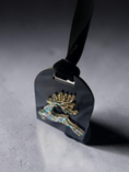 Load image into Gallery viewer, A close-up of a black acrylic ornament featuring a gold pine tree with iridescent blue and green rhinestone reindeer accents, hanging from a black ribbon against a gray textured background.