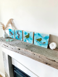 Charger l'image dans la visionneuse de la galerie, Four square handmade wood cradles depicting mirror birds on a blue alcohol ink background, displayed on a rustic wooden mantel with decorative seashells and a vase.