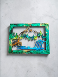 Load image into Gallery viewer, Handmade resin and wood wall art featuring a bear, mountain peaks, and a waterfall in an emerald green and gold marbled frame.
