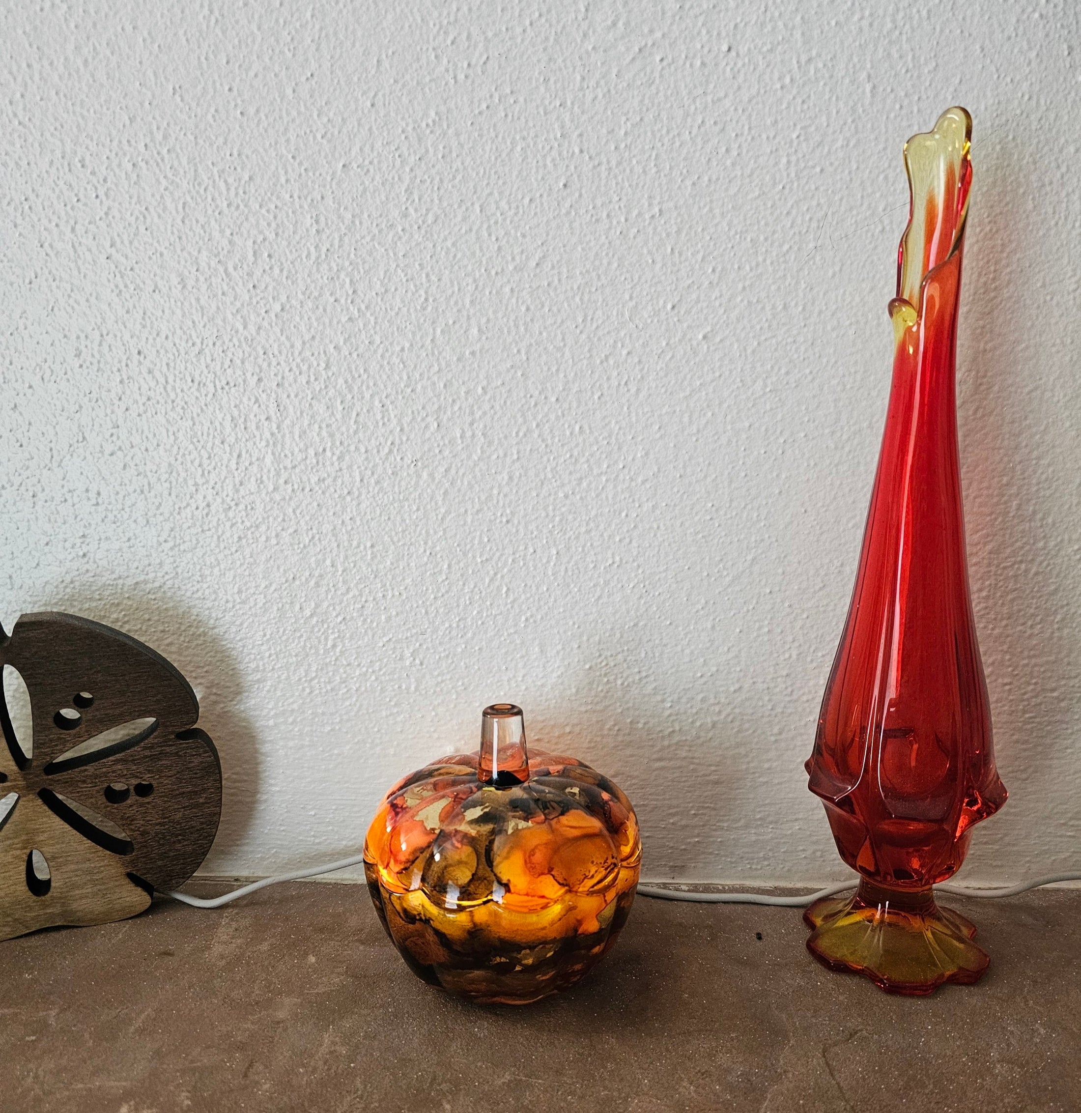 Coastal Elegance Decor handcrafted ink glass pumpkin dish with amber and orange swirls next to a tall red glass vase.