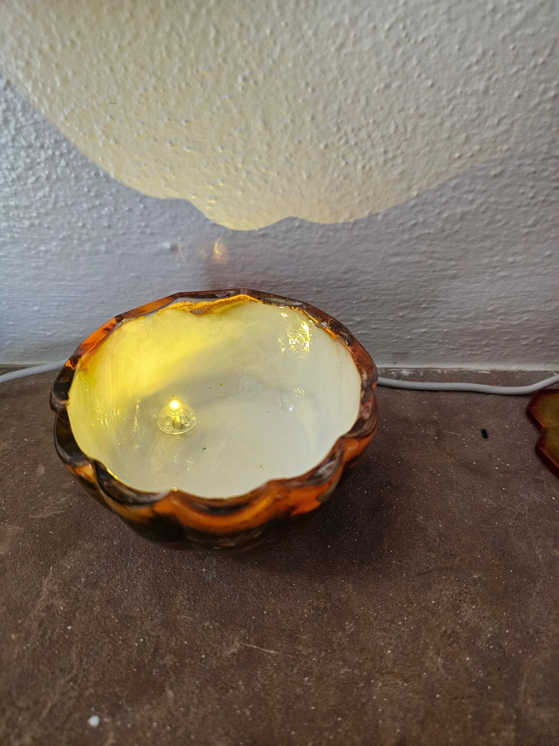 Coastal Elegance Decor handcrafted glass pumpkin dish with amber and orange ink swirls, illuminated by a tea light.