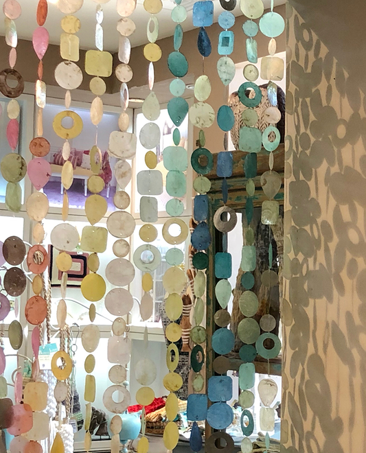 A decorative hanging of Capiz Shell Single Strand Indoor or Outdoor Decoration, featuring a mix of colorful shells casting unique shadows, perfect for enhancing interior spaces.