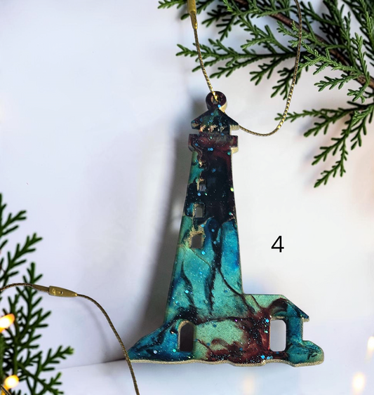Turquoise and red handmade lighthouse resin and wood ornament on a white background with Christmas lights and boughs 
