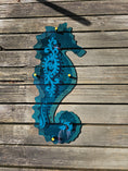 Load image into Gallery viewer, Large teal acrylic seahorse mounted with standoffs, projecting vibrant turquoise light and dancing reflections onto a sunroom wall.
