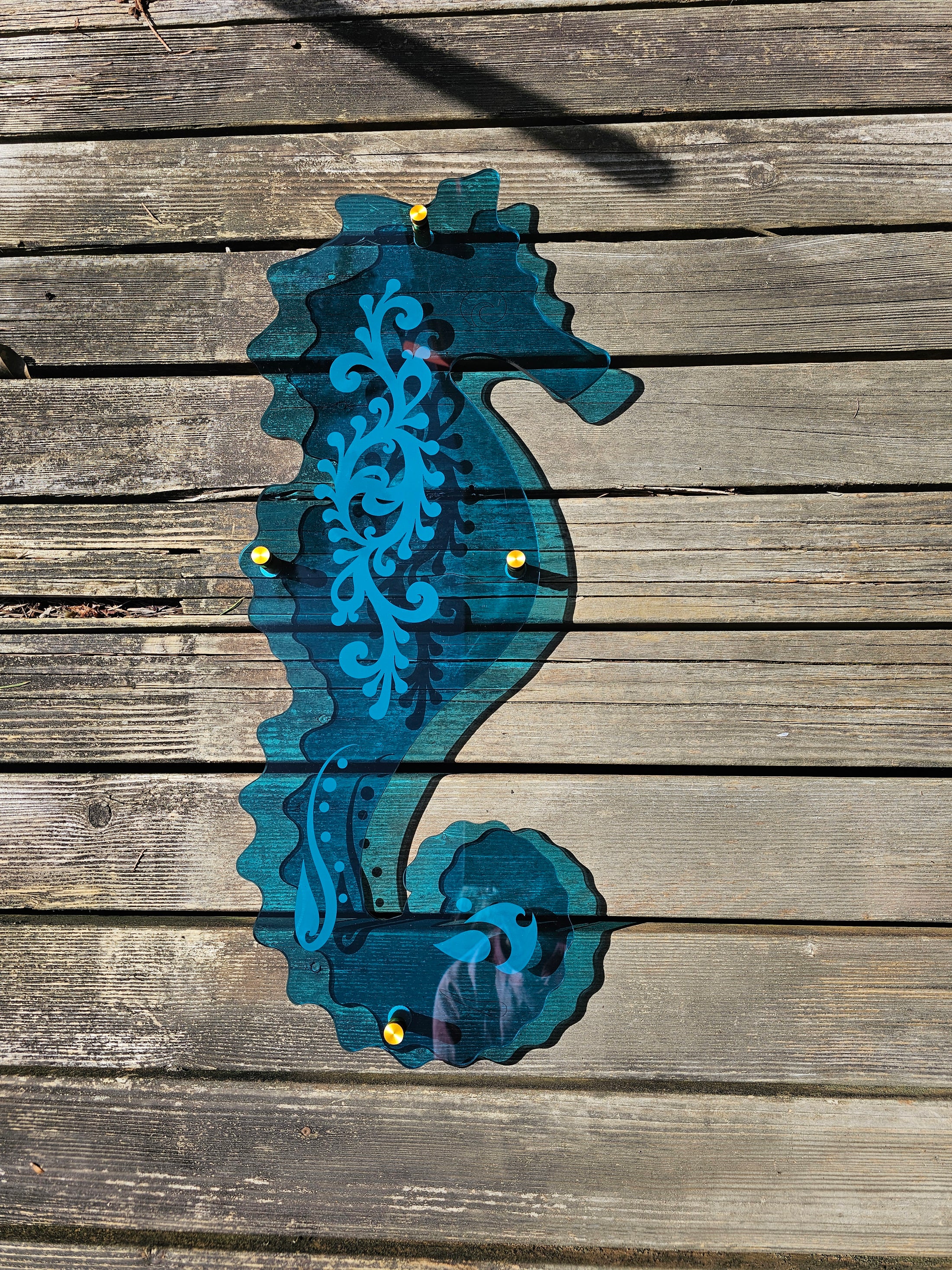 Large teal acrylic seahorse mounted with standoffs, projecting vibrant turquoise light and dancing reflections onto a sunroom wall.