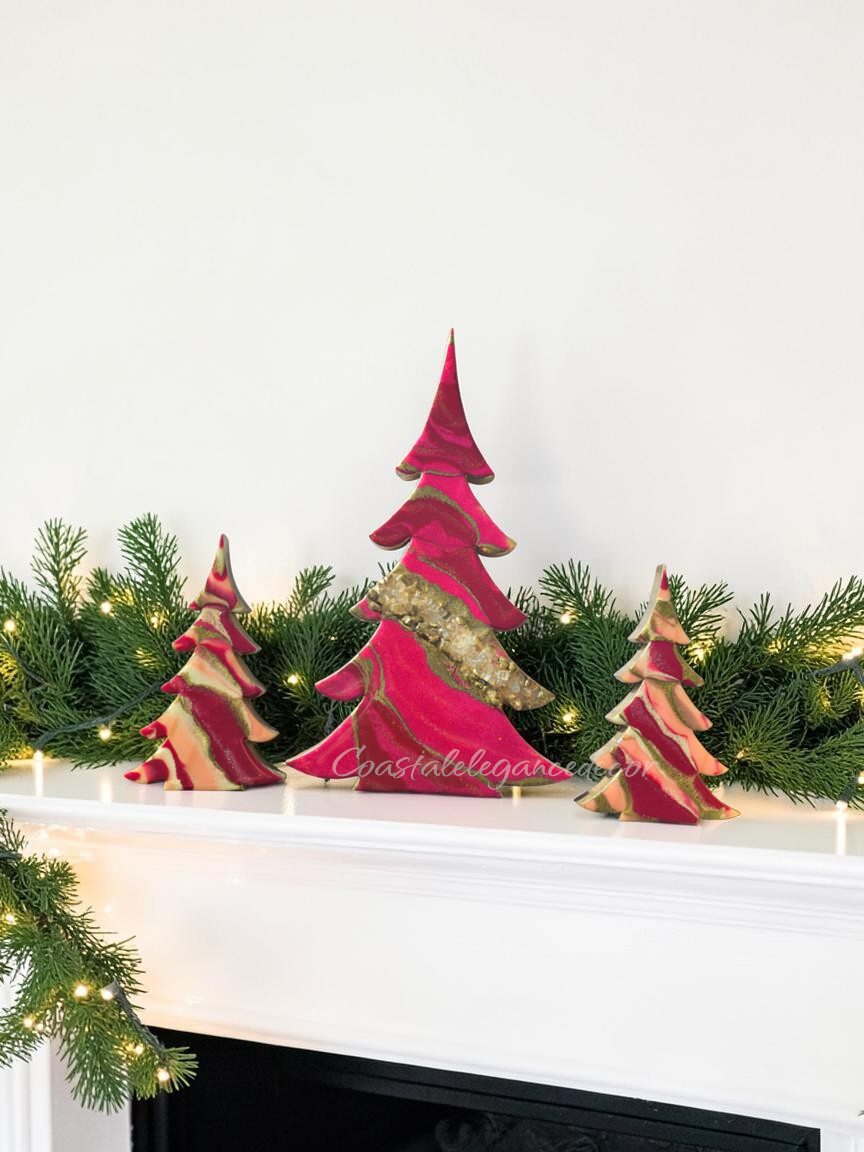 A set of handcrafted solid pine Christmas trees decorated with hand-poured swirling cranberry, fuchsia, and ivory fluid resin. The tall center tree features a diagonal band of crushed glass geode texturing with gold and glitter accents