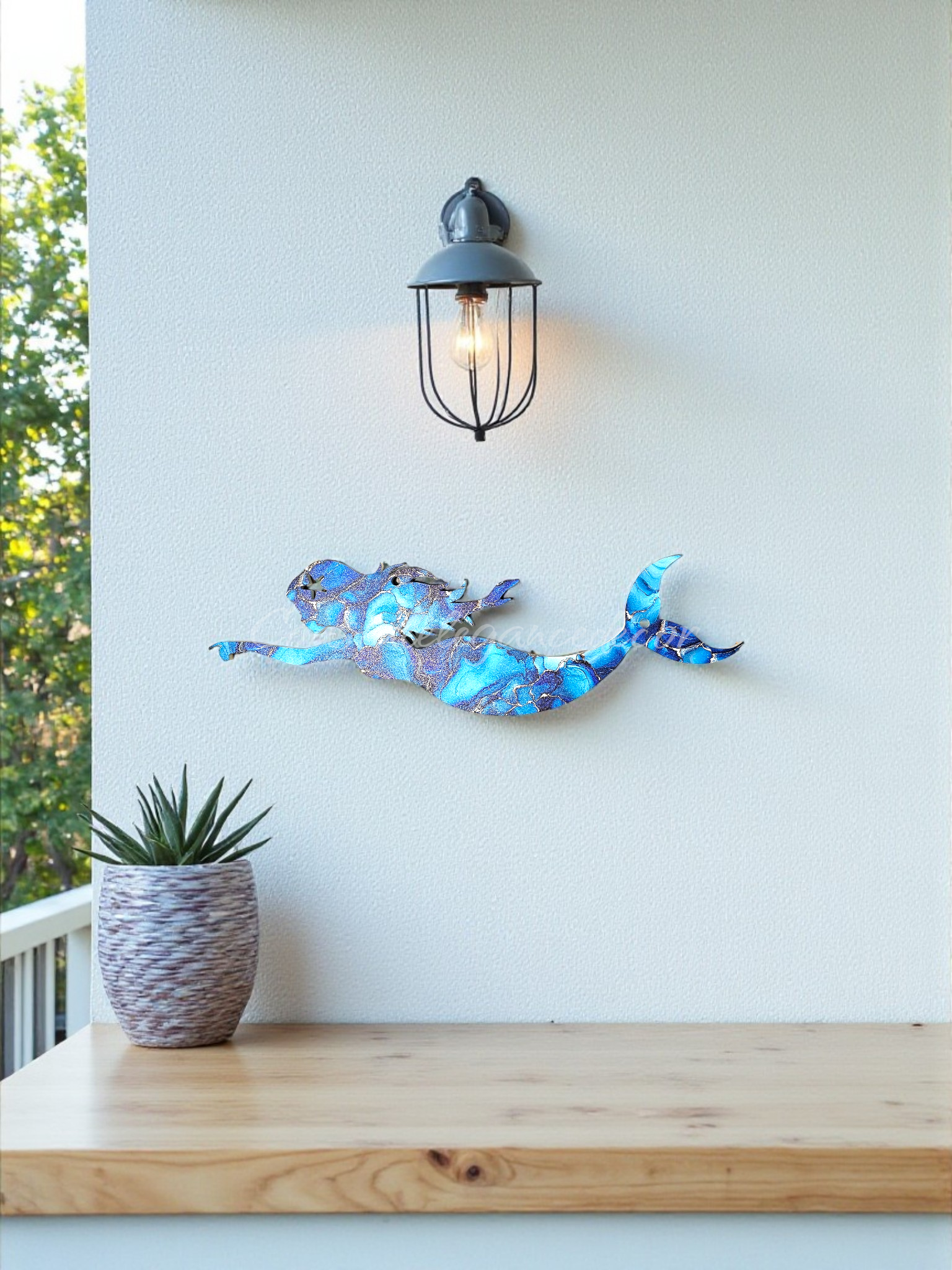 Blue marbled swimming mermaid hanging on a white porch wall with a small plant