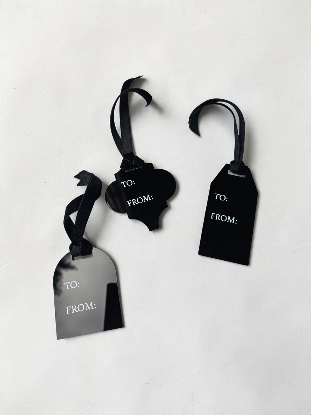 Three black gift tags with black ribbon loops and white 'TO:' and 'FROM:' text, arranged on a plain white background.