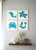 Load image into Gallery viewer, Four square tiles with blue sea-themed designs on a wall above a wooden shelf.
