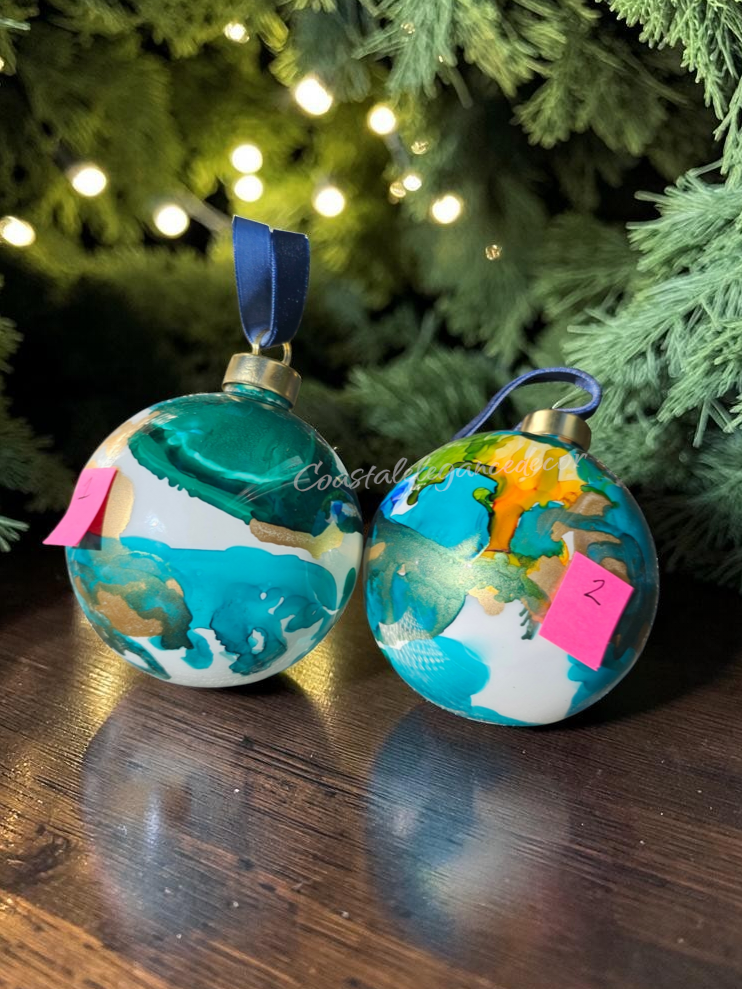 Handmade glass balls with teals, ocean blues and orange highlighted with gold metallic sitting on a warm wood table
