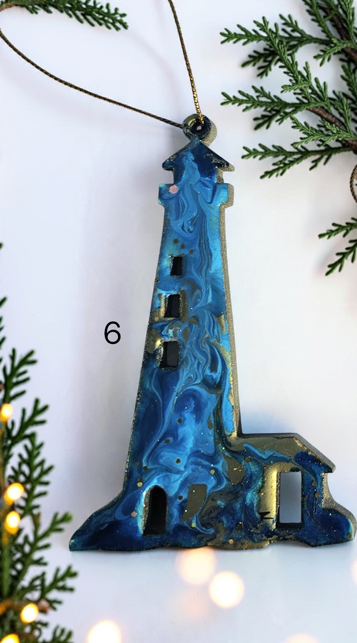 Blue swirl handmade lighthouse resin and wood ornament on a white background with Christmas lights and boughs 