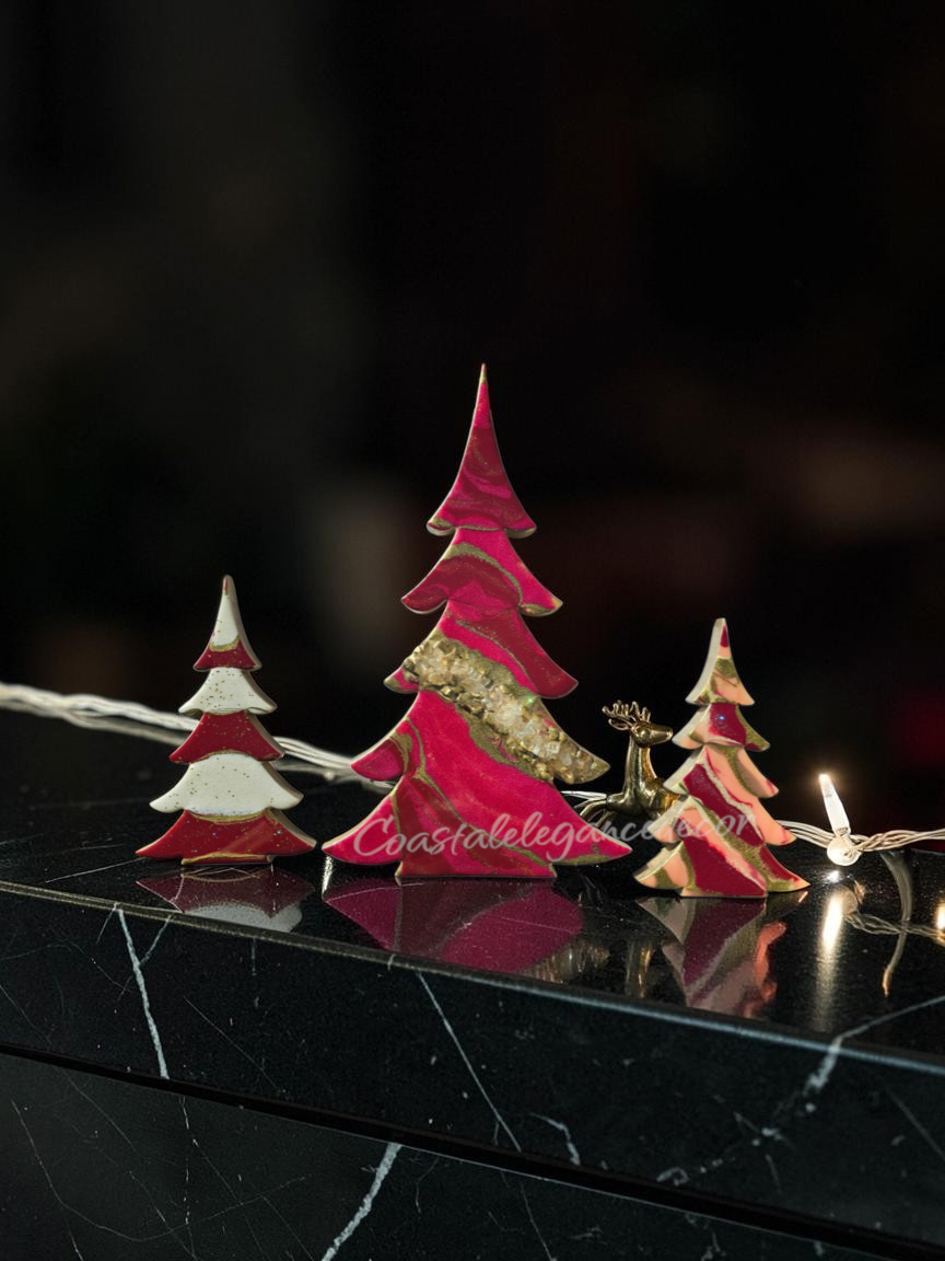 A set of handcrafted solid pine Christmas trees decorated with hand-poured swirling cranberry, fuchsia, and ivory fluid resin. The tall center tree features a diagonal band of crushed glass geode texturing with gold and glitter accents,