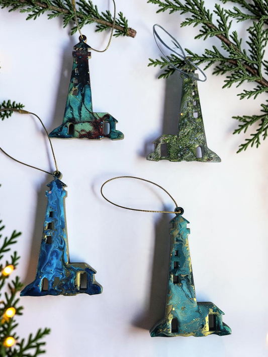Four handmade lighthouse resin and wood ornaments on a white background with Christmas lights and boughs 