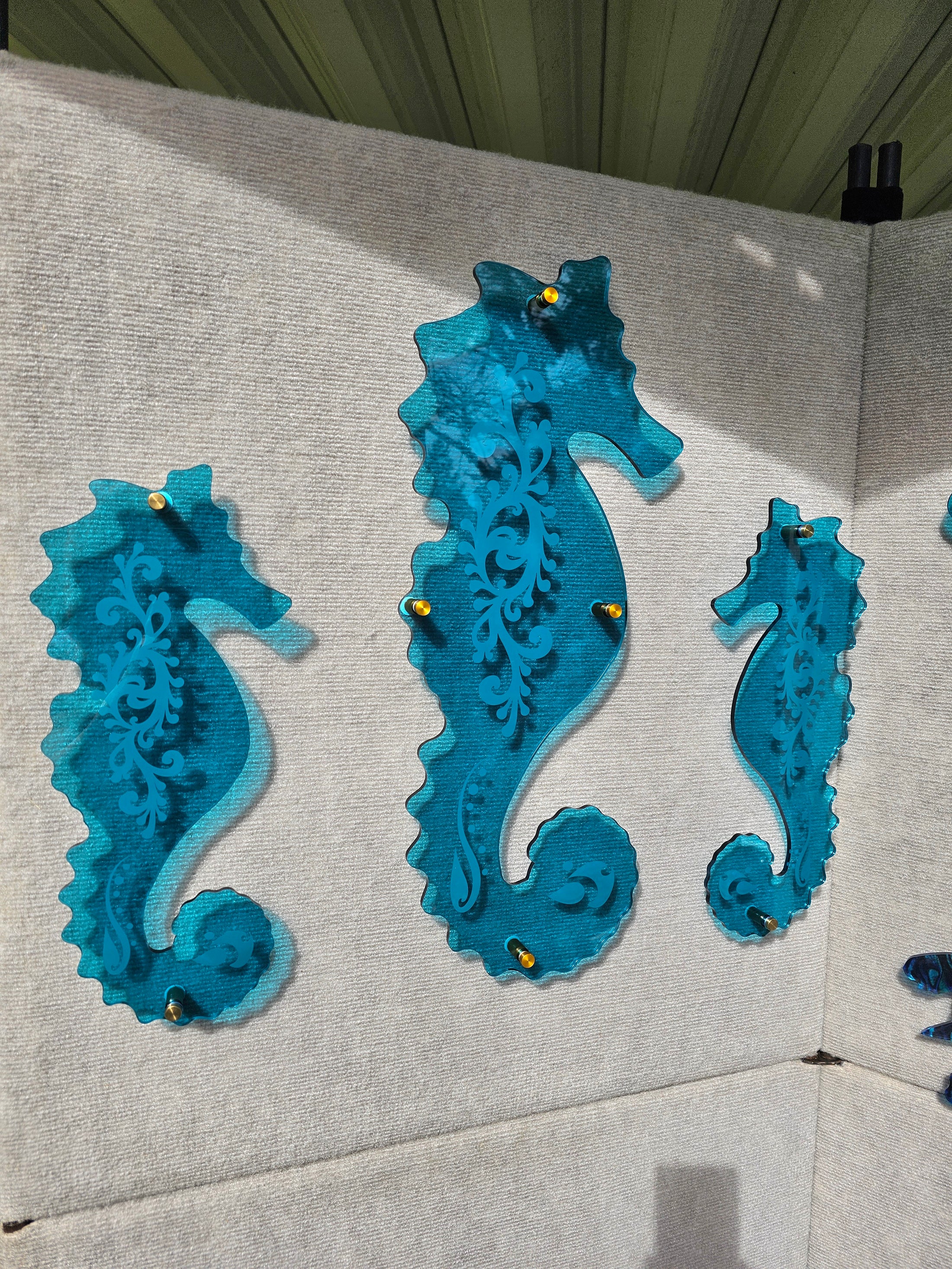 Three vivid tranparent teal acrylic seahorses with custom engraved pattern mounted with gold toned standoffs 