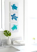 Load image into Gallery viewer, Three blue turtle sculptures on a white wall above a sink with a green leaf and white vase.
