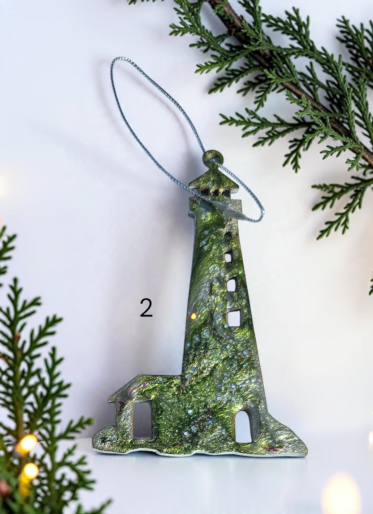 Green handmade lighthouse resin and wood ornament on a white background with Christmas lights and boughs 